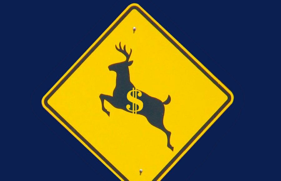 Road sign with silhouette of jumping deer and dollar sign in the center.