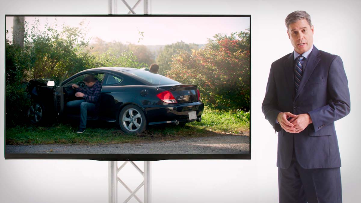 Detective in a suit and tie next to a large TV showing a car accident.